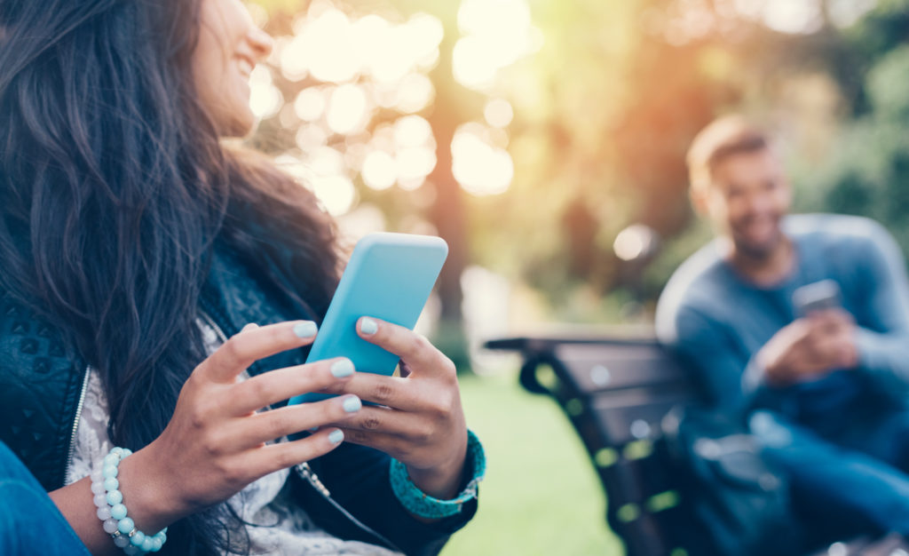 Flirting couple in the park texting on smartphones